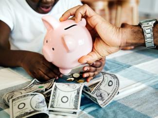 Hand holding piggy bank over a pile of money