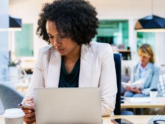 Woman looking at phone in front of an open laptop