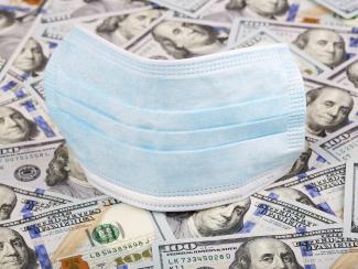 Medical face mask on the top of hundreds of US dollar bank notes