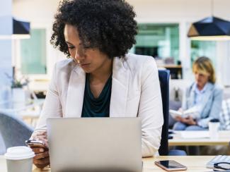 Woman looking at phone in front of laptop