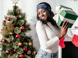 Woman holding present in front of Christmas tree