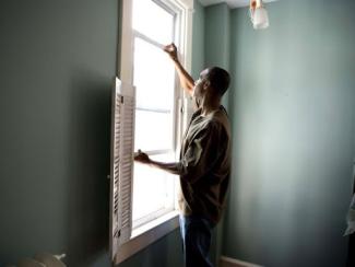 black man fixing shutters on a window