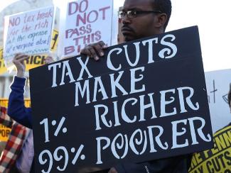 Demonstrator holding "Tax Cuts Make 1% Richer 99% Poorer" sign