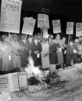Black and White shipping clerks strike in front of a fire for better wages and union recognition.