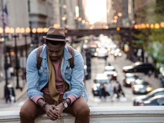 Man sitting on bridge with head down and hands folded