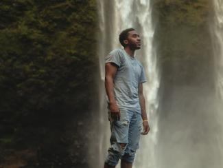 black man standing outside by a waterfall