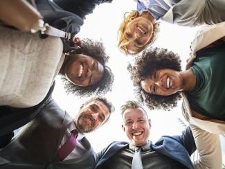 group of people in business wear looking down in a circle and smiling