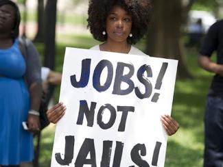 black woman holding a sign that says jobs not jails