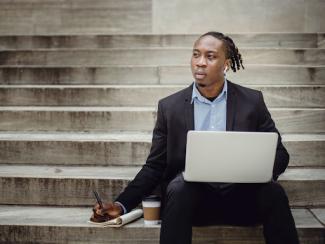 thoughtful black worker using netbook and taking notes on steps