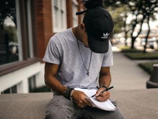 person sitting on a ledge writing in an open notebook