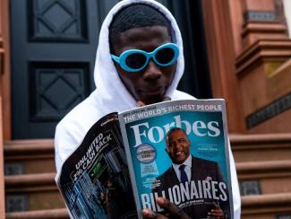 black man holding a forbes magazine outside