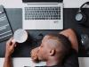 black man asleep at desk with cup in hand and laptop open