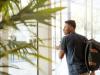 black man looking outside window carrying black and brown backpack while holding his hand on the window